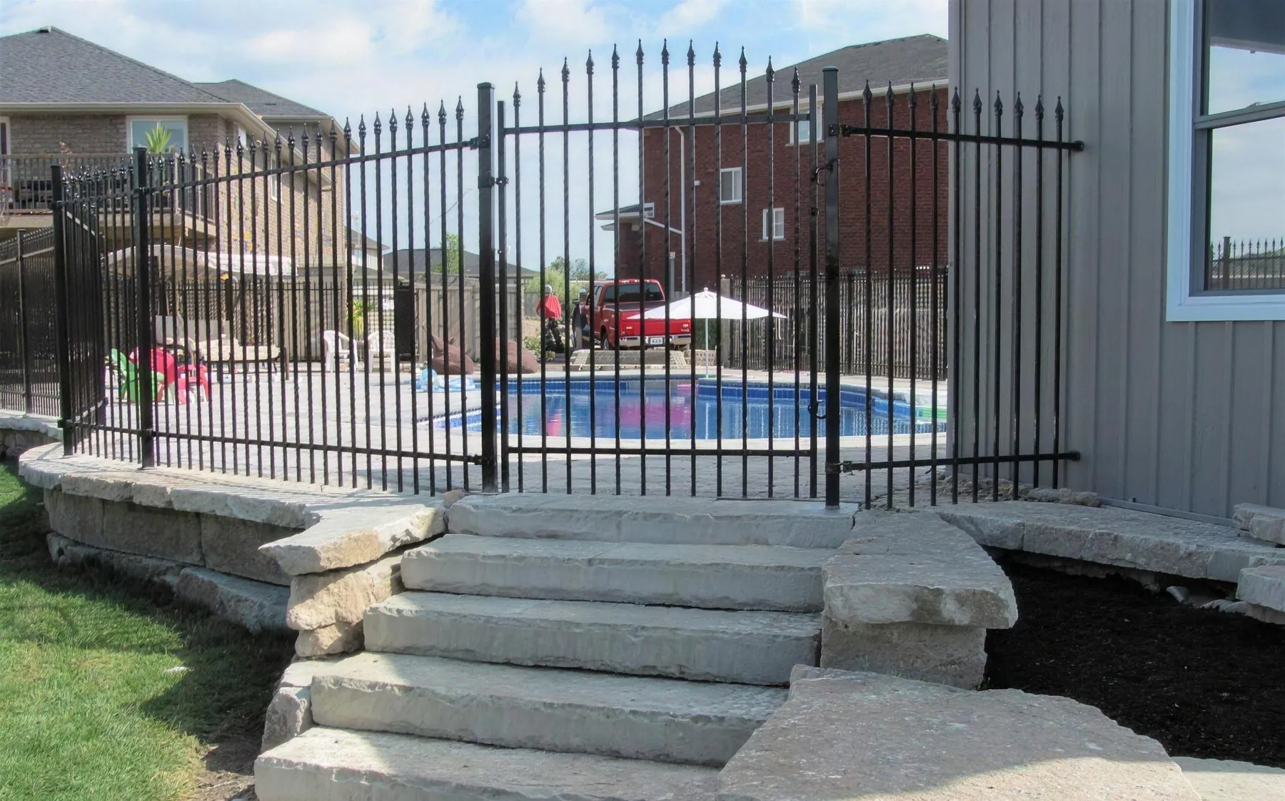 Black ornamental iron pool fence with a self-closing gate beside a stone patio