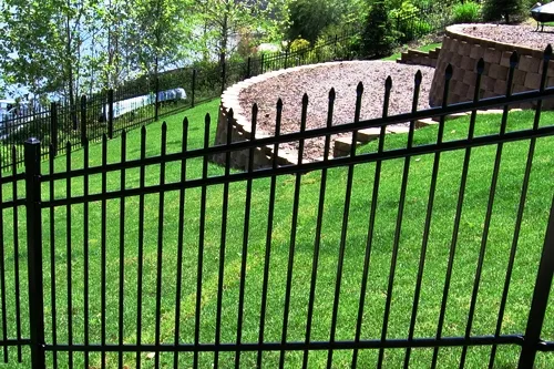 Ornamental iron pool fence with self-latching gate at the top of stone steps leading to a backyard pool
