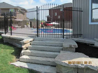 Code-compliant black ornamental iron pool fence surrounding an in-ground pool with stone landscaping in the Peterborough area