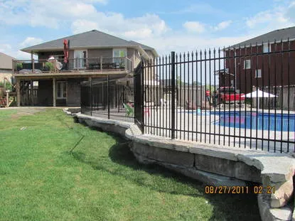 Iron pool fence following a curved stone retaining wall around a backyard pool